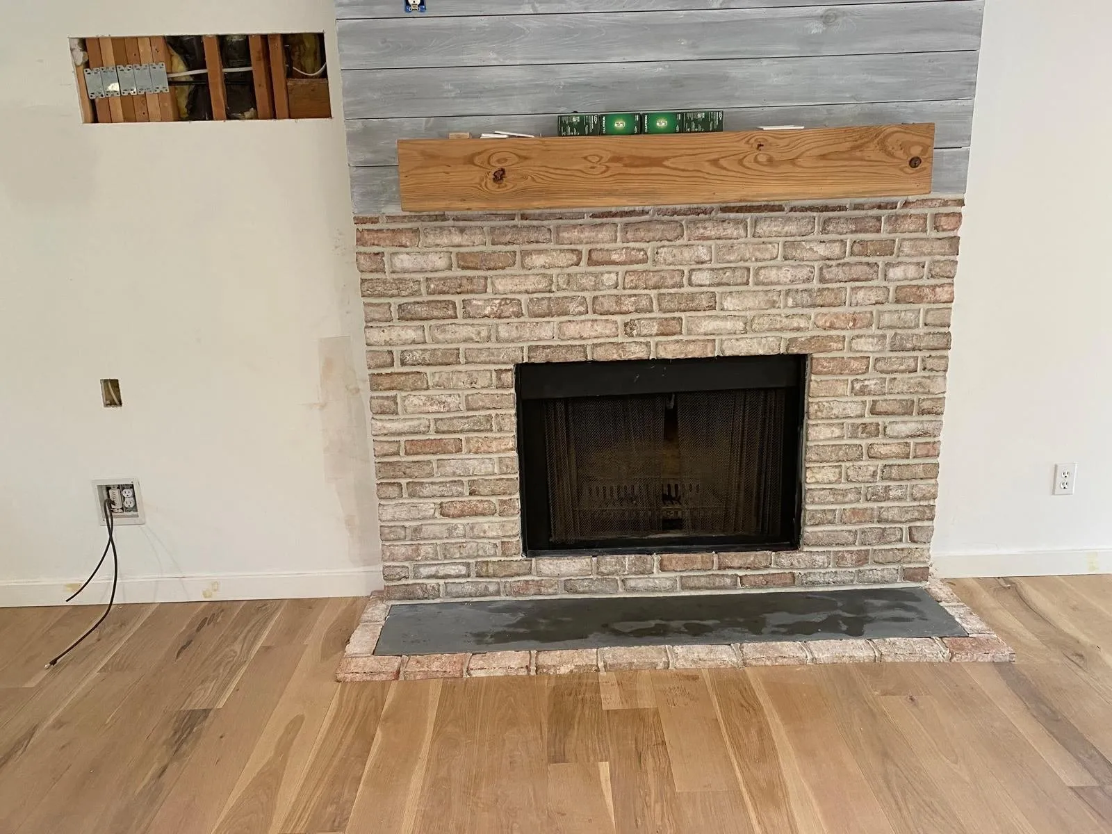 Whitewashed brick fireplace with a reclaimed wood mantel and hardwood floor
